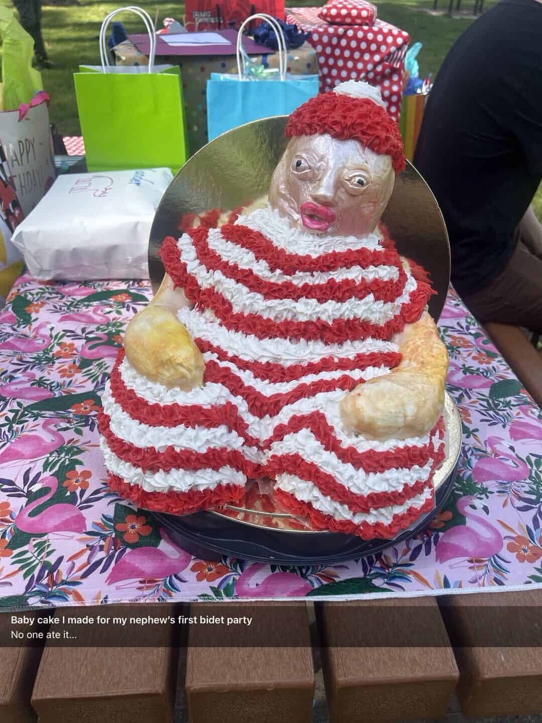 A horrifying "baby cake" for a "first bidet party" with a shiny, unsettling face and a striped outfit.