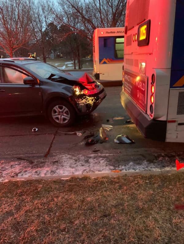 The aftermath of a car accident, showing a grey SUV with a smashed front end after hitting a bus.