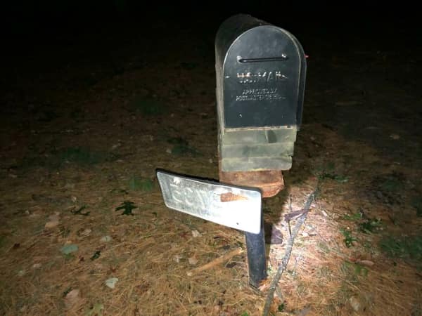 A mailbox at night with a bent license plate stuck to its post after a hit-and-run.