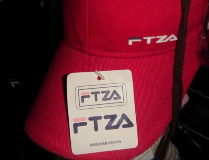 A red baseball cap showing a funny knock off brand of Fila that just says "FTZA."