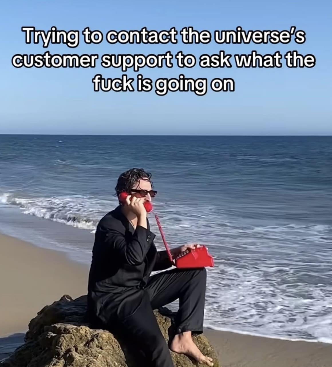 Funny reaction meme of a person on a beach with a red phone, "Trying to contact the universe's customer support."