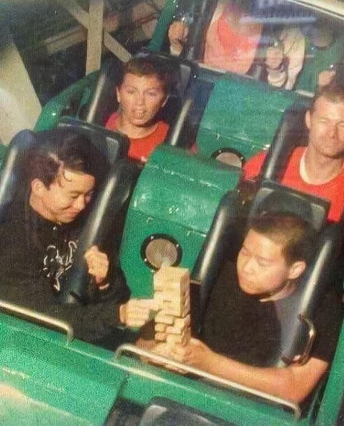 A hilarious, staged funny rollercoaster picture of two men calmly playing a game of Jenga on the ride.
