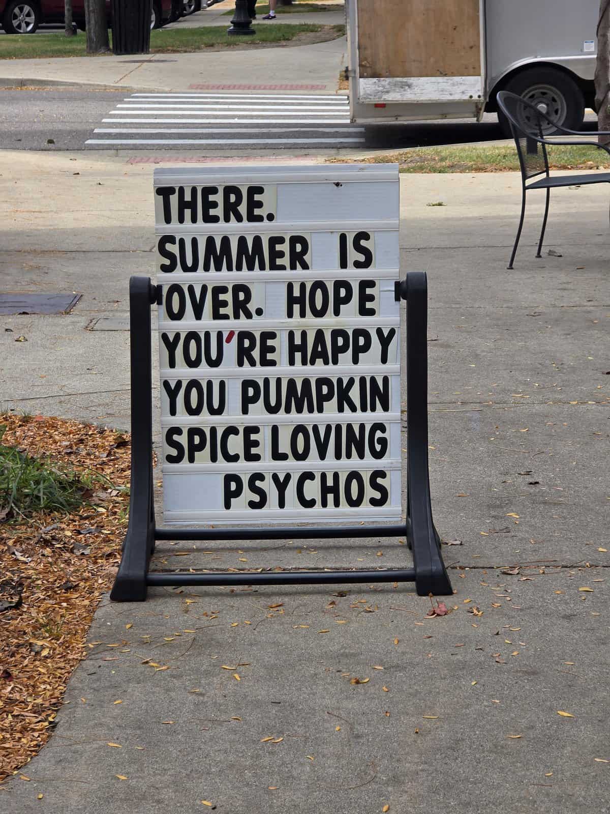 A funny sign on a sidewalk A-frame, roasting "pumpkin spice loving psychos" now that summer is over.