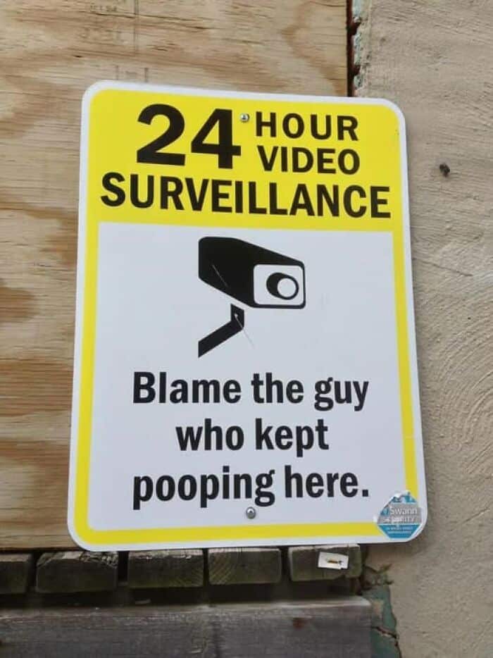 A surveillance camera warning sign that blames "the guy who kept pooping here."