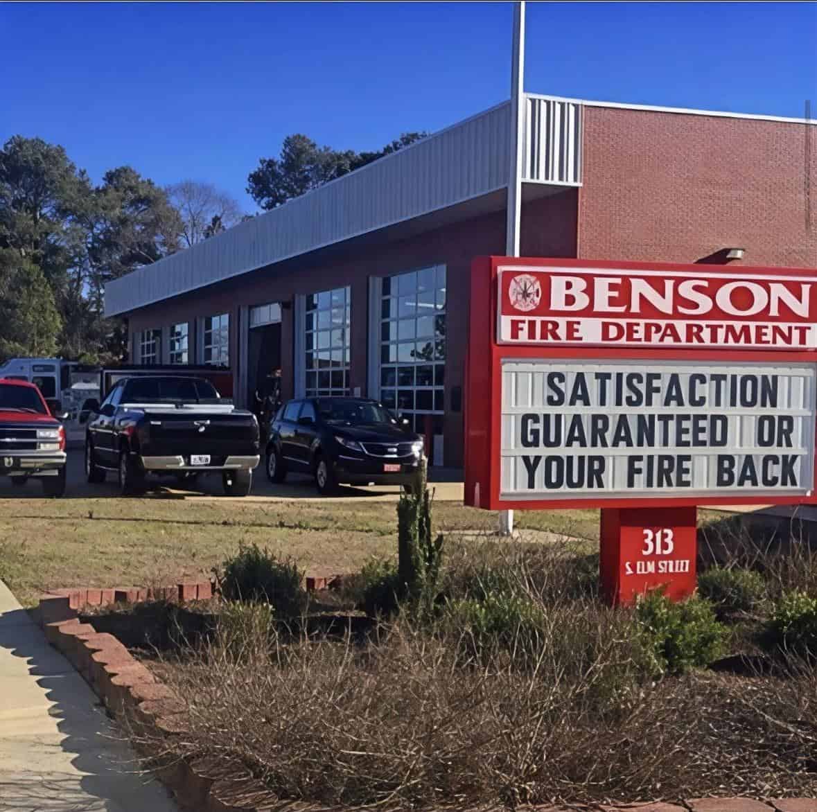 A funny sign outside a fire department offering "Satisfaction Guaranteed Or Your Fire Back."