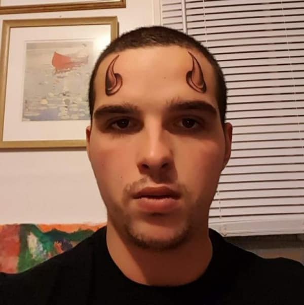 Small shaded devil horns tattooed on a man's forehead above the eyebrows.
