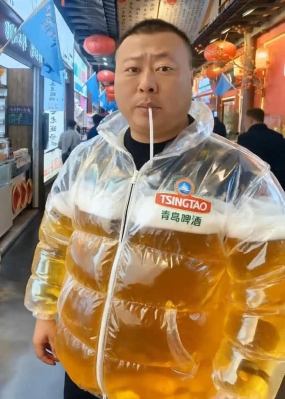 A hilarious meme of a man wearing a clear puffer jacket that is filled with beer, which he is drinking with a straw