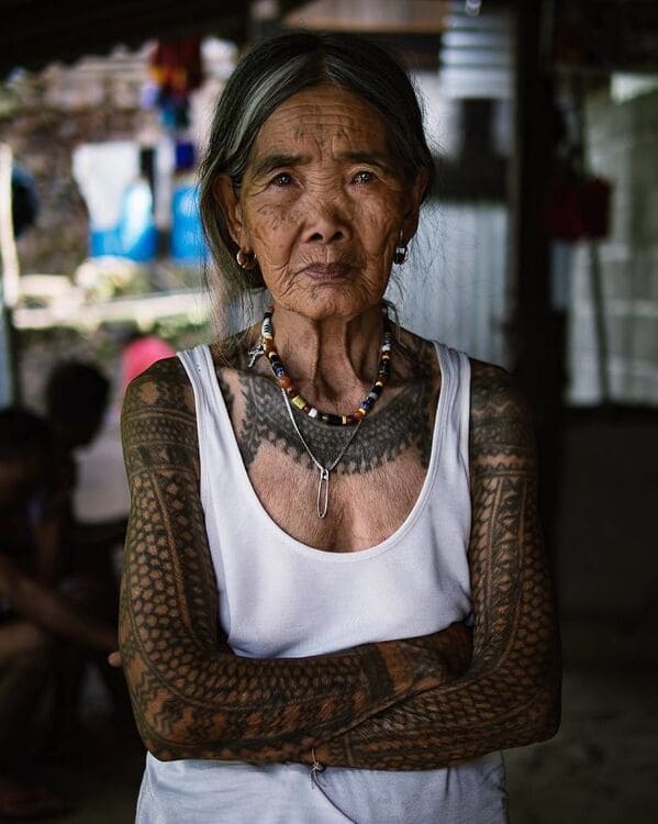 A striking photo of an elderly indigenous woman with traditional, full-sleeve and chest tattoos.