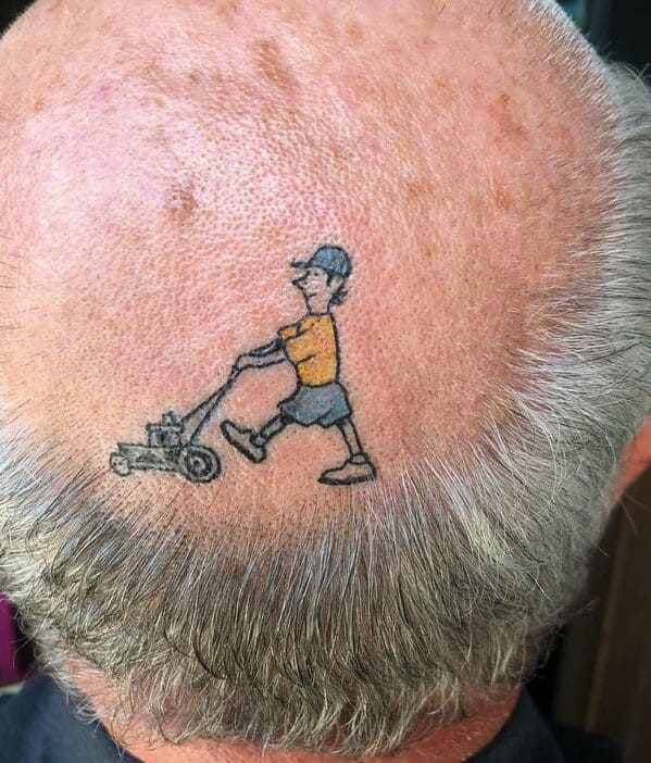 A hilarious, small cartoon tattoo on a balding man's head of a man mowing his "lawn" of grey hair.