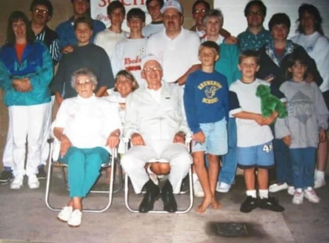Awkward family photo with an optical illusion where the man in the chair appears to have a woman's legs.