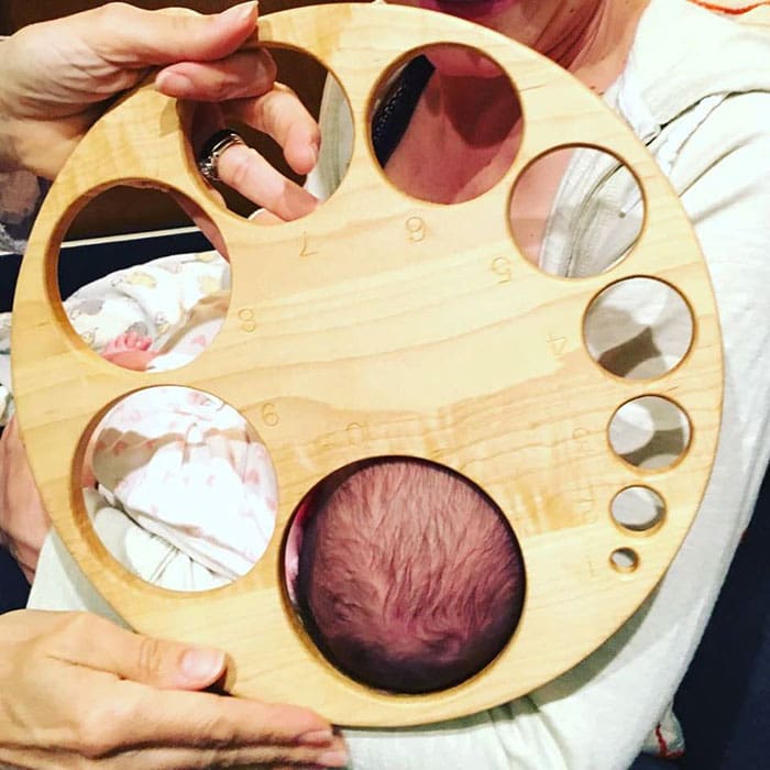 Wooden board with different sized holes representing cervical dilation stages during labor.