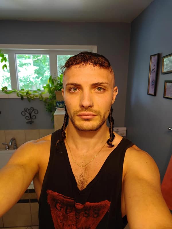 A man with a bizarre haircut featuring short curly bangs and two long, thin braids on the sides.