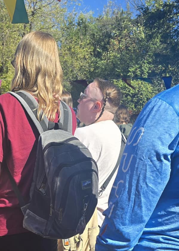 A man at a fair with a "rat tail" style haircut, featuring a single, long braid in the back.