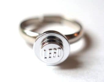 A minimalist and nerdy silver ring featuring a single, classic, shiny LEGO stud as the gem.