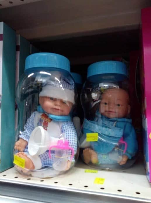 Plastic baby dolls stuffed inside clear plastic jars on a store shelf.
