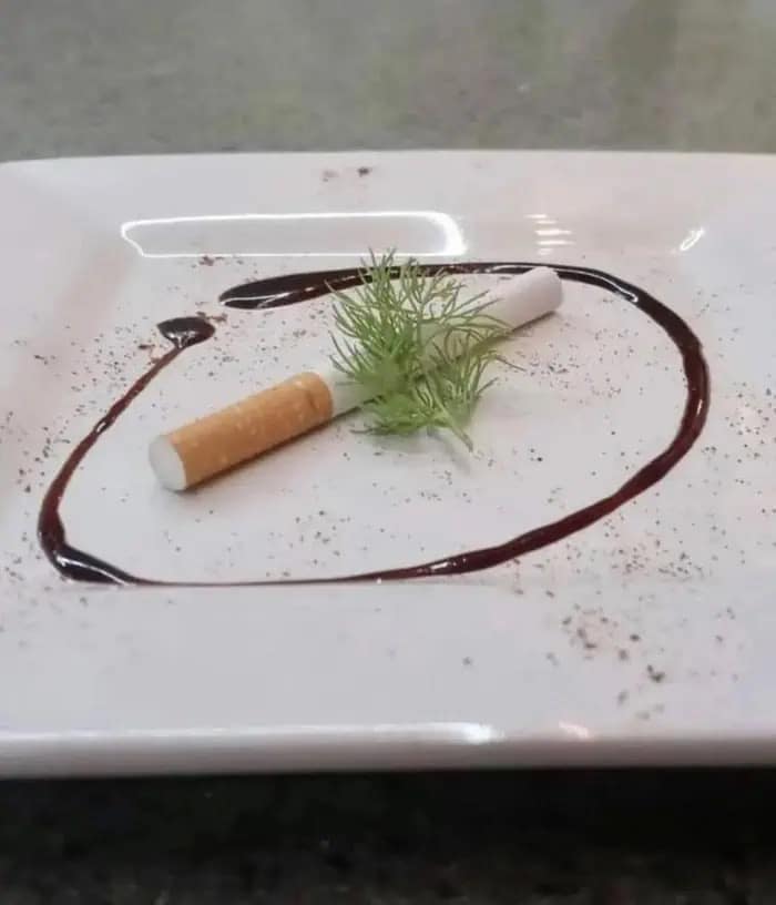 A funny meme showing a cigarette plated like fine dining with garnish and sauce.