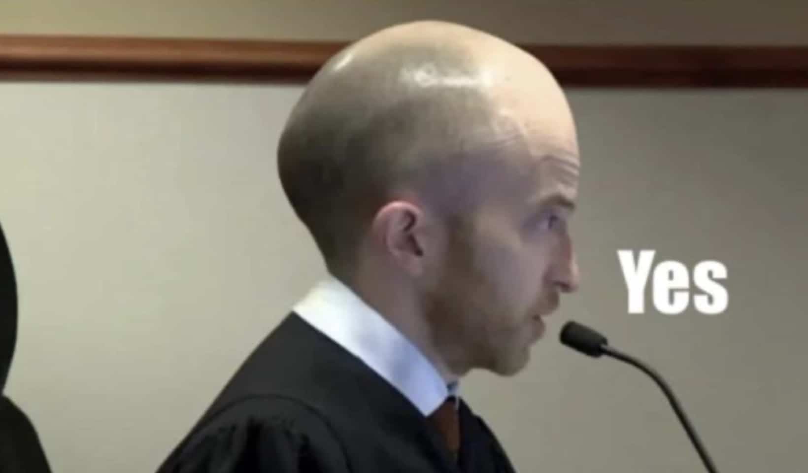 A funny side profile of a bald man speaking into a microphone with the word yes on screen.