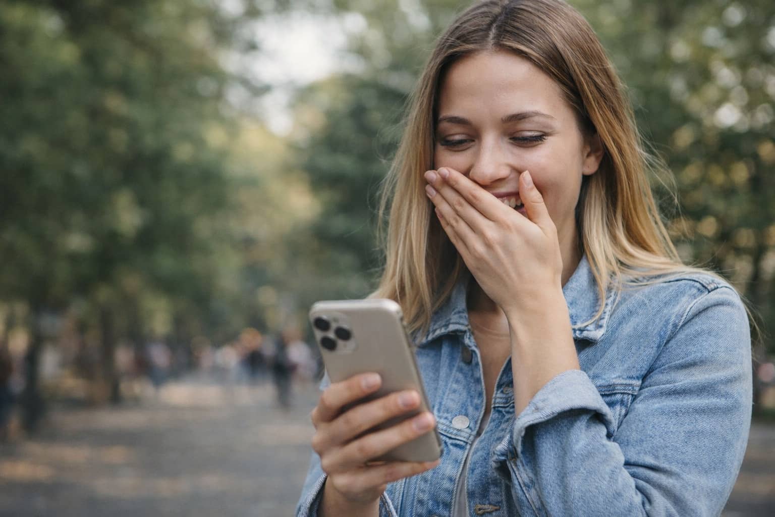 Young woman laughing at her phone screen while outdoors, perfect for funny names meme reaction.