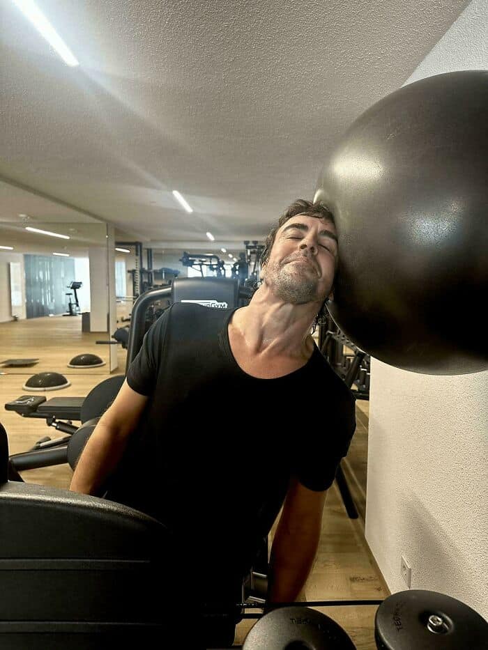 Formula 1 driver Fernando Alonso performing a neck strength exercise with a large exercise ball.