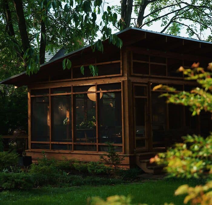 Screened in backyard wooden gazebo glowing with warm interior light at dusk. Cool diy woodworking projects.