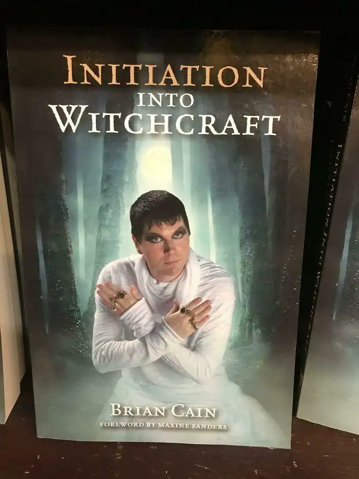 A non-fiction book cover for "Initiation into Witchcraft" featuring a man in white robes and heavy eye makeup.