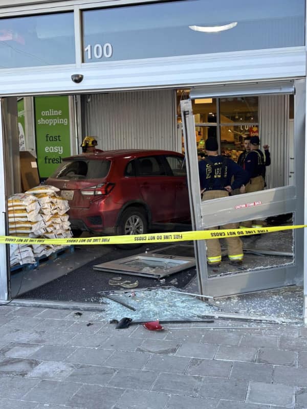 car fail: A red Mitsubishi SUV crashed through the glass entrance of a grocery store with firefighters and yellow caution tape on site