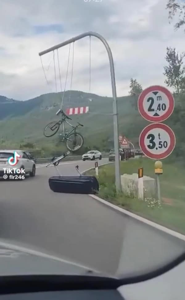 driving fail: A bicycle and a car roof storage box dangling precariously from an overhead utility pole arm above a busy highway