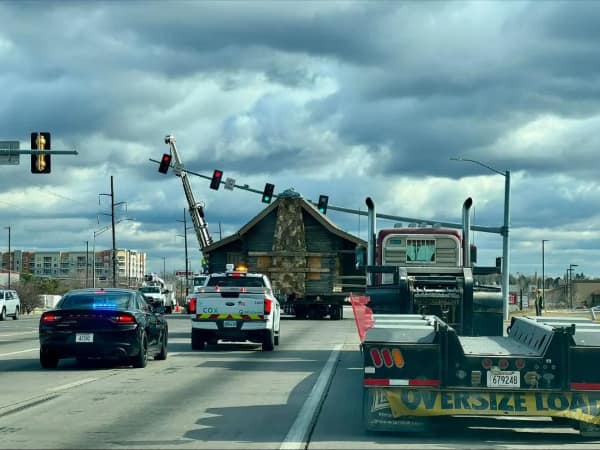 driving fail: A semi-truck transporting an entire log cabin hitting and bending an overhead traffic light pole across a multi-lane road