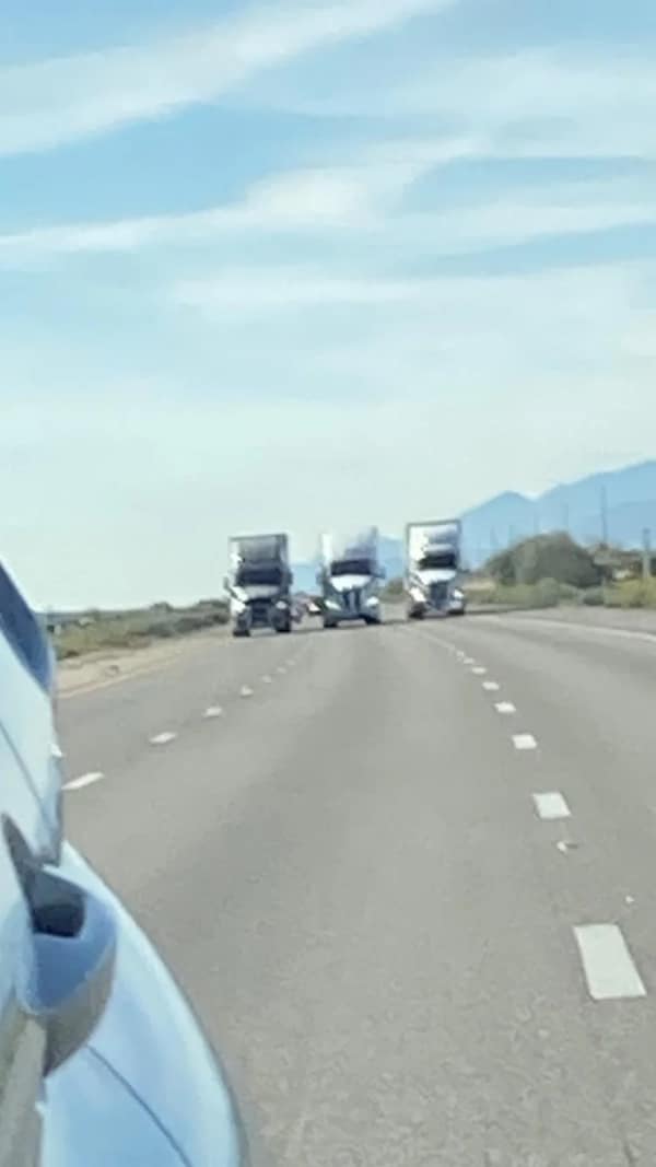 driving fail: Three large semi-trucks driving perfectly side-by-side across all lanes of a highway, preventing any other vehicles from passing