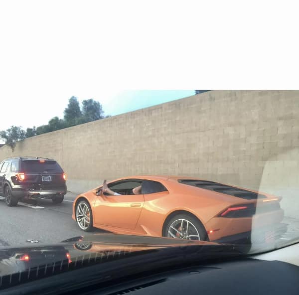 driving fail: An orange Lamborghini supercar in traffic with the driver resting their bare foot outside the window on the side-view mirror
