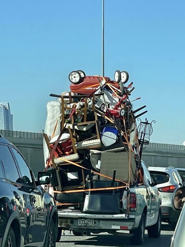 Alt Text: car fail: A white pickup truck on a highway carrying a massive, precarious mountain of furniture and household goods