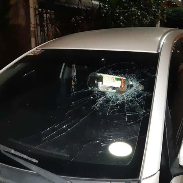 car fail: A full glass bottle of liquor smashed through the center of a white car's front windshield