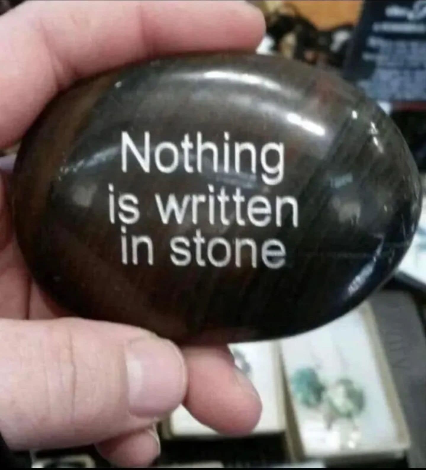 Hand holding a dark polished rock engraved with the ironic phrase nothing is written in stone in this classic meme.