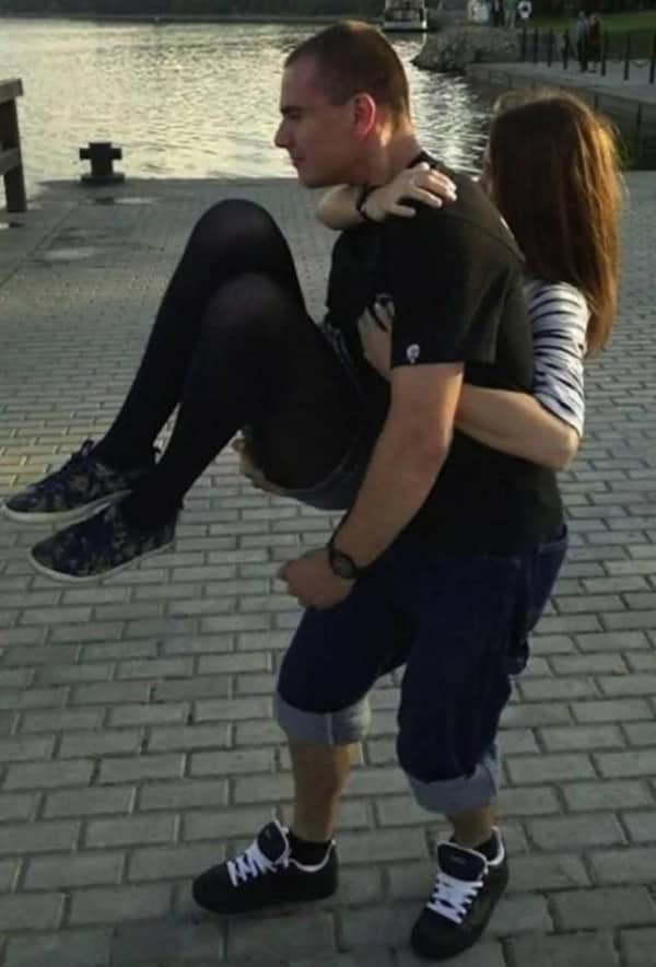 Man carrying a woman whose black leggings make it look like he has tiny legs.