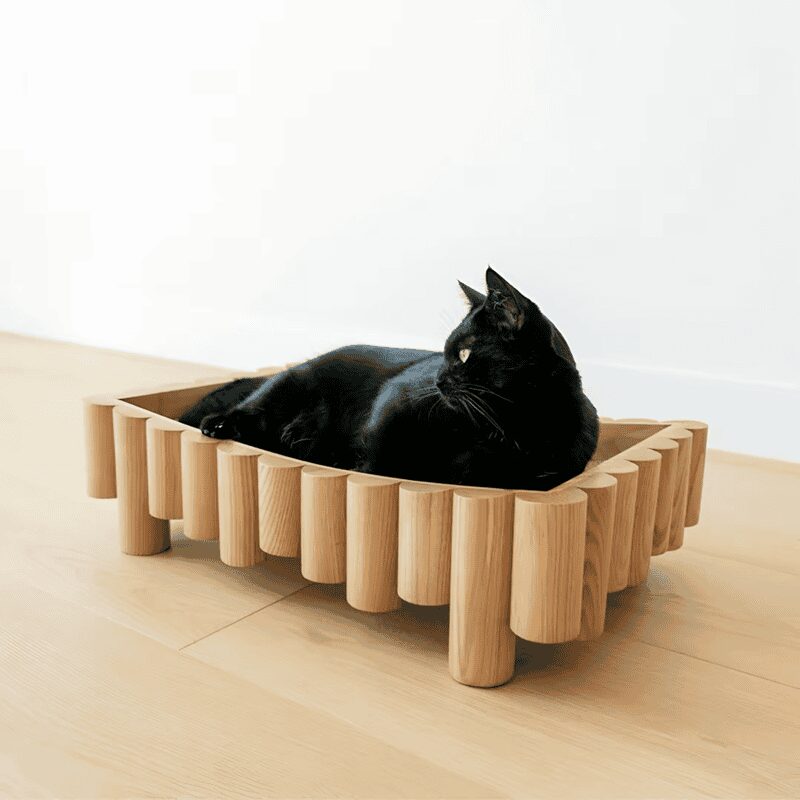 Unique cat bed made of vertical wooden dowels with a black cat lounging comfortably inside.