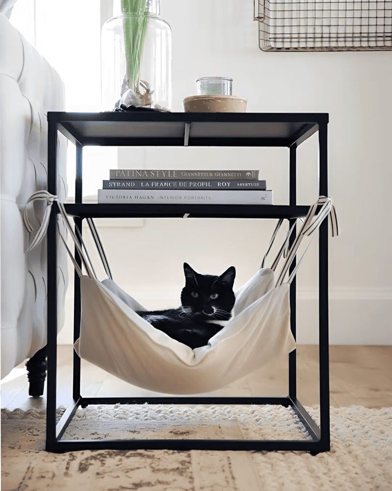 Black metal side table with a built-in white fabric cat hammock used by a tuxedo cat.