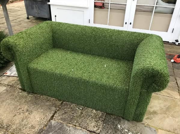 A cursed furniture armchair completely covered in artificial green grass, bringing the outdoors uncomfortably inside the living room.