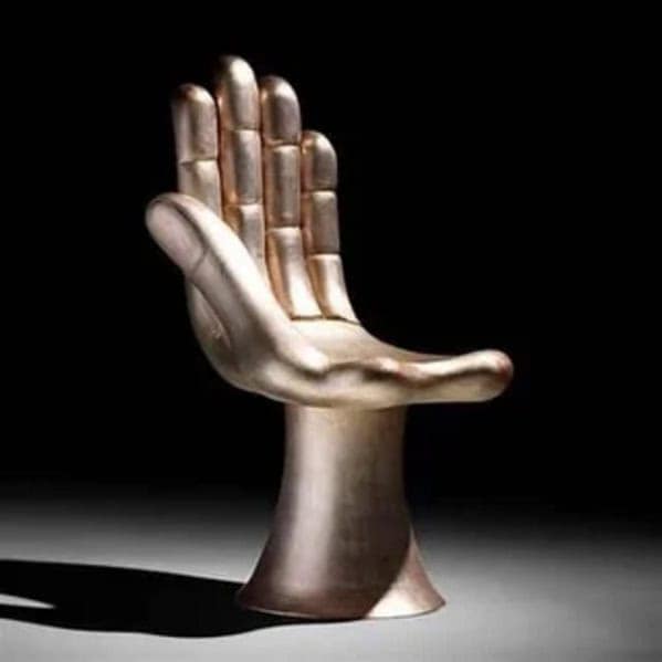 A weird furniture chair shaped like a giant, metallic human hand with the palm forming the seat and fingers acting as the backrest.