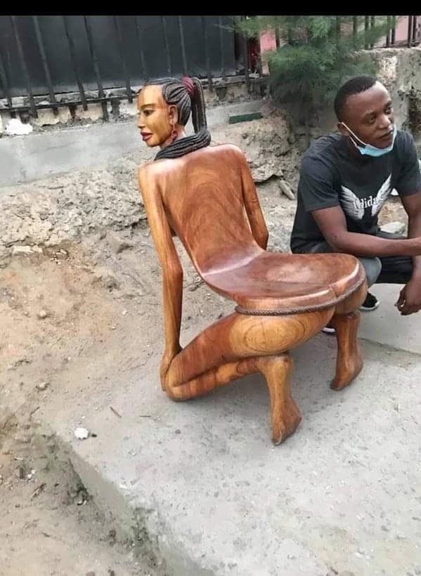 A cursed furniture wooden chair carved in the shape of a woman in a contorted kneeling position, with the seat resting on her back.