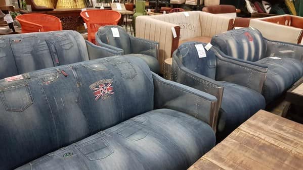 A cursed furniture collection featuring a sofa and armchairs fully upholstered in recycled blue jeans, complete with pockets, seams, and belt loops known as a "jouch."
