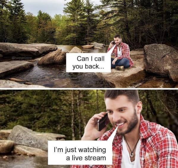 Man in a red plaid shirt sitting on rocks by a stream, talking on his phone.