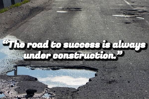 A cracked asphalt road with puddles and a demotivational quote about the road to success.