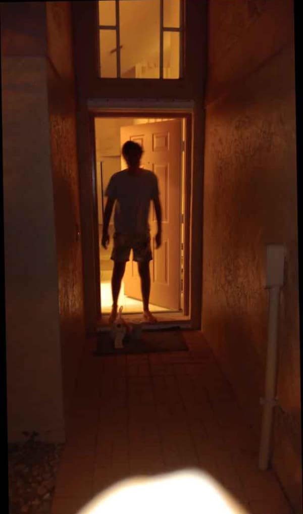 A funny doordash photo showing a delivery driver standing in a dark doorway looking like a horror movie villain waiting for the customer to open the door.