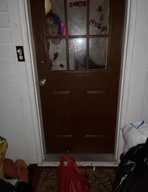 A door dash meme showing a drop-off photo where the customer is staring through the glass door surrounded by terrifying Halloween decorations saying help and danger.
