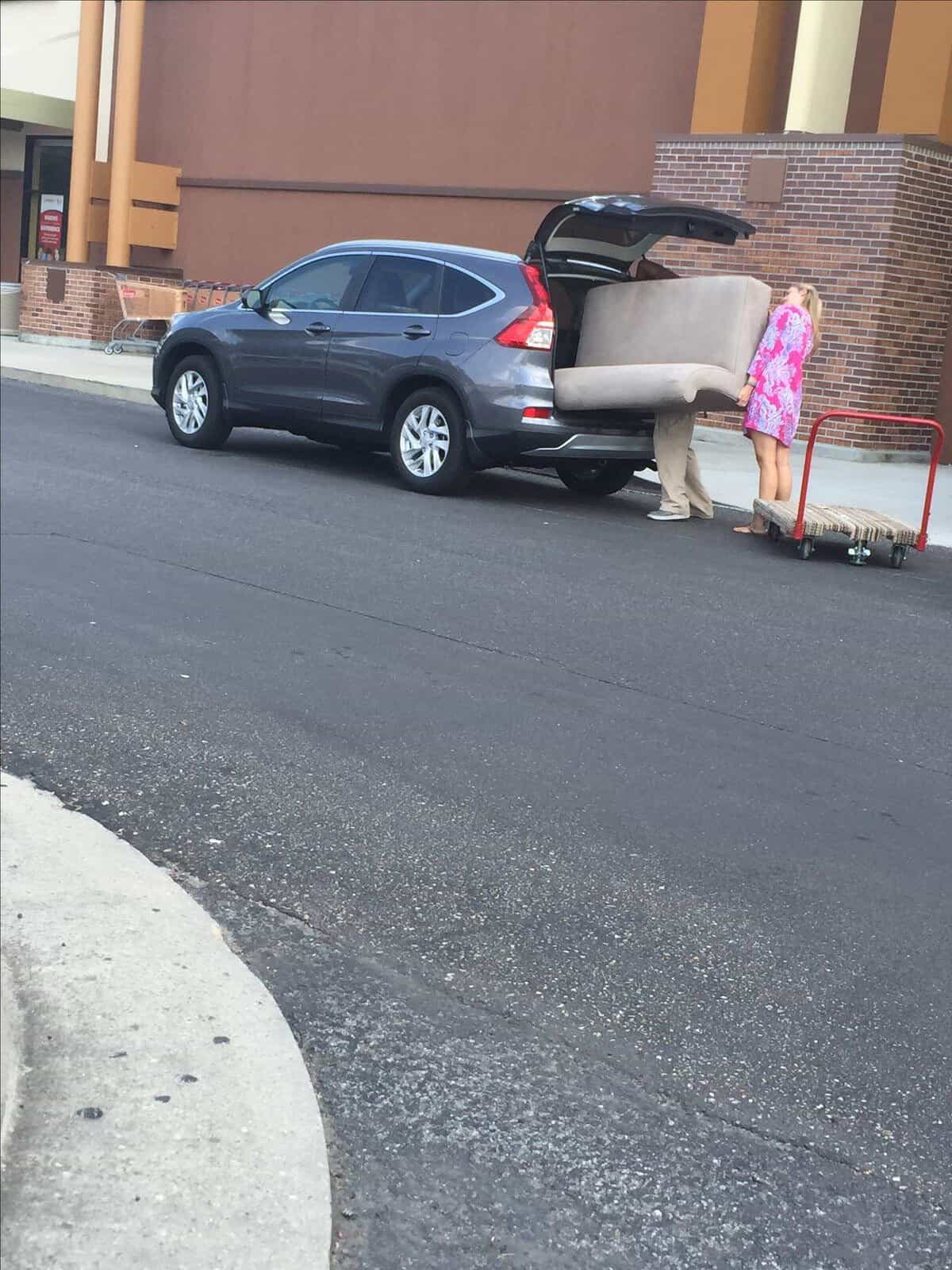 Two people attempting to fit a massive couch into the back of a small SUV.