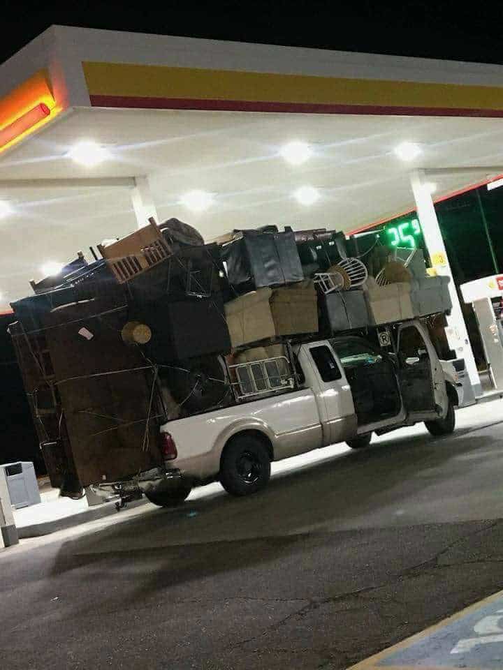 White pickup truck at a gas station dangerously overloaded with an entire household of furniture.