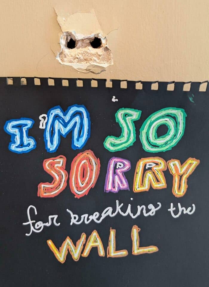 Hand-drawn colorful sign featuring two holes in a wall with an apology for the damage.