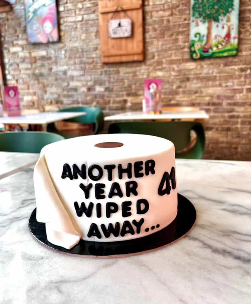 A funny cake shaped like a roll of toilet paper with the pun text Another year wiped away to celebrate a 41st birthday.