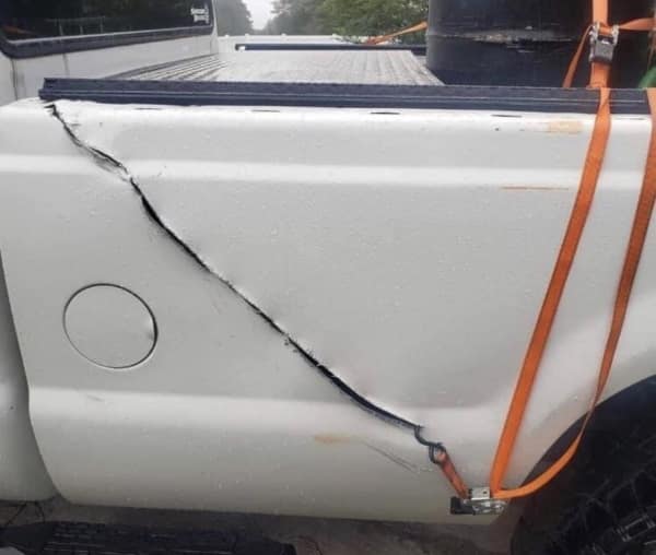 A terrible DIY moving bad day photo showing the side of a white pickup truck completely crumpled and torn open because the owner hooked a heavy-duty ratchet strap directly to the thin sheet metal.