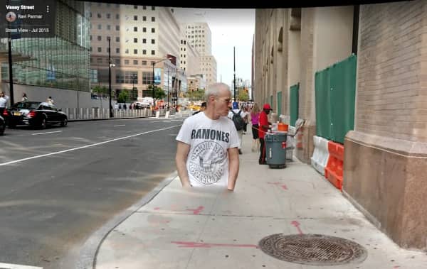 A man wearing a Ramones t-shirt appearing half-submerged in a concrete city sidewalk.
